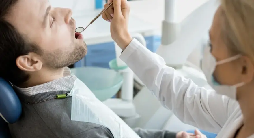 Pacjent u dentysty, zastanawia się, ile kosztuje wizyta u dentysty prywatnie. Lekarz bada jego zęby.