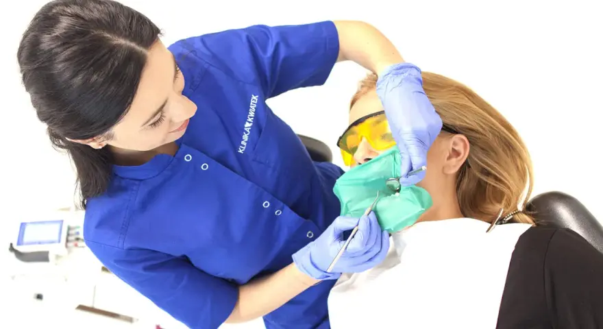 Dentystka zakłada koferdam, zieloną osłonę izolującą ząb pacjentki. To nowoczesne rozwiązanie w stomatologii.